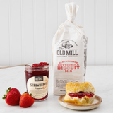 Old Mill biscuit mix bag with a biscuit and strawberry preserves on a white surface.